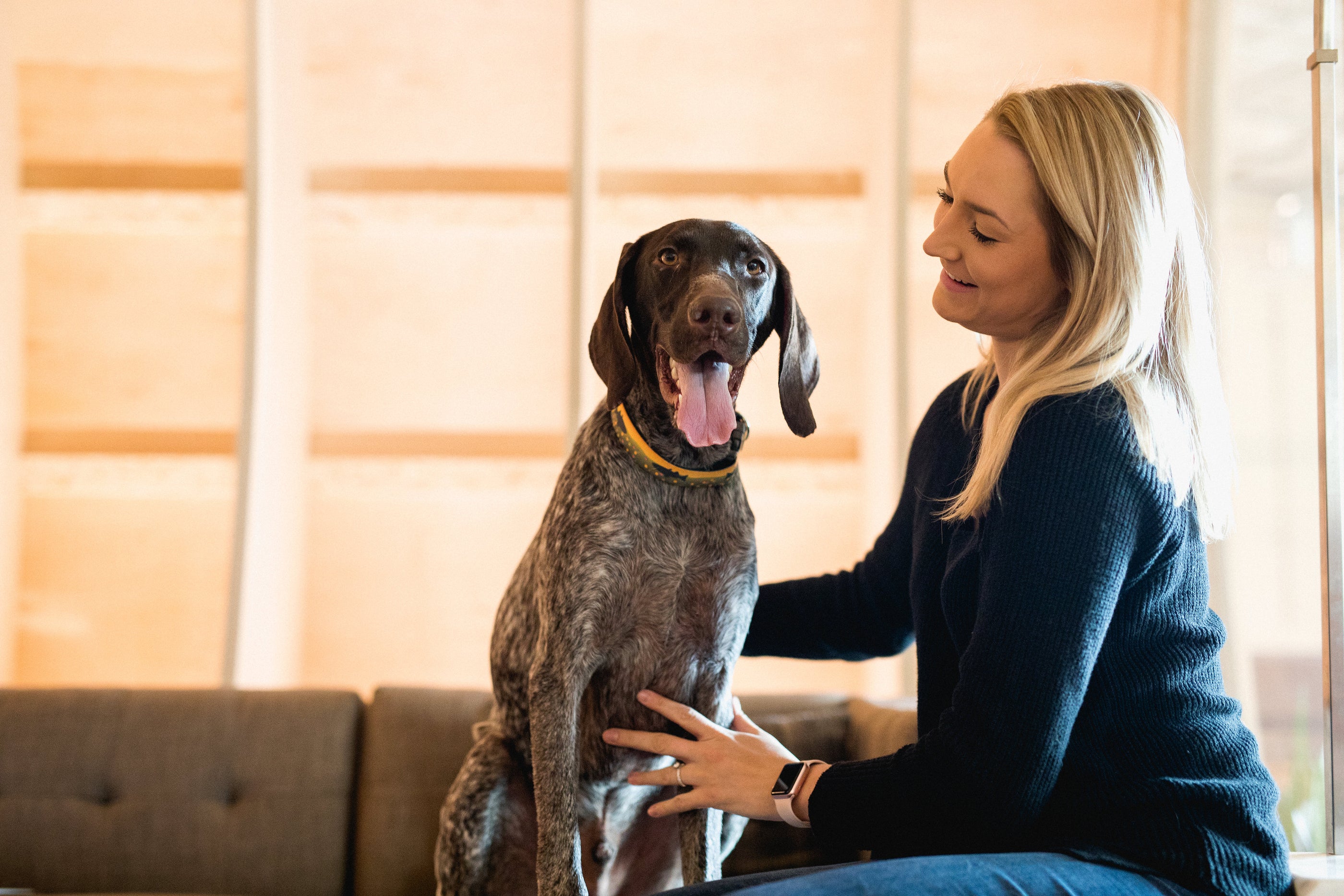 A woman petting a dog with its tongue out.