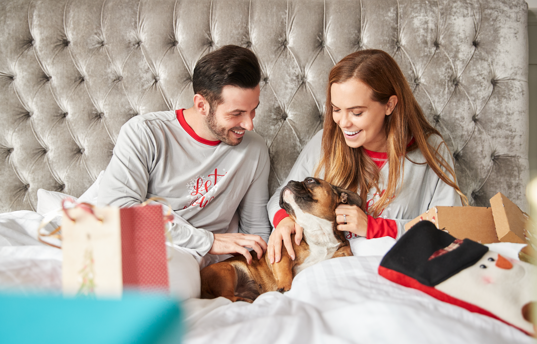 A man and woman in pajamas petting a dog on a couch.