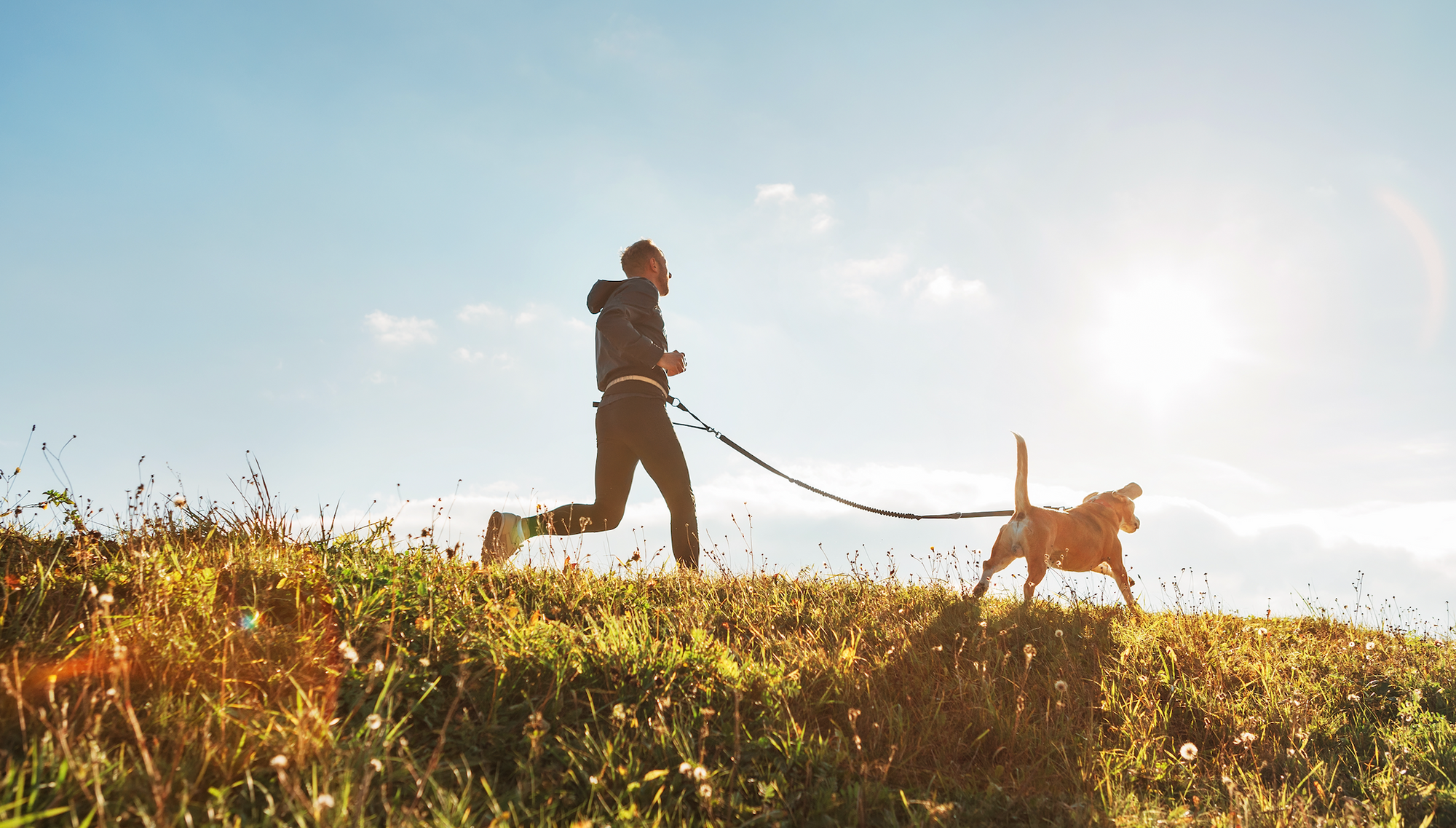 A man running with a dog on a leash in a grassy field.