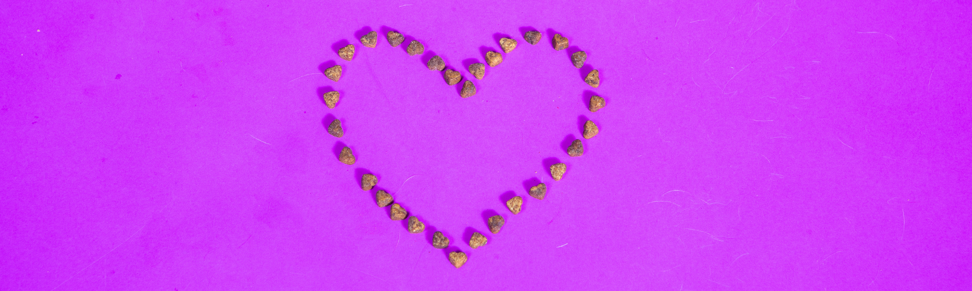 A heart shape made up of small brown stones is arranged neatly against a vibrant purple background.