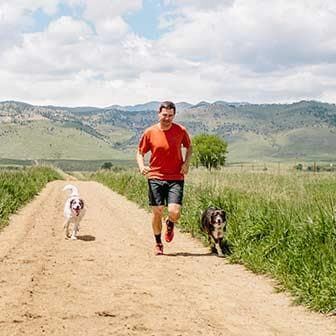 A man running with two dogs on a dirt road.